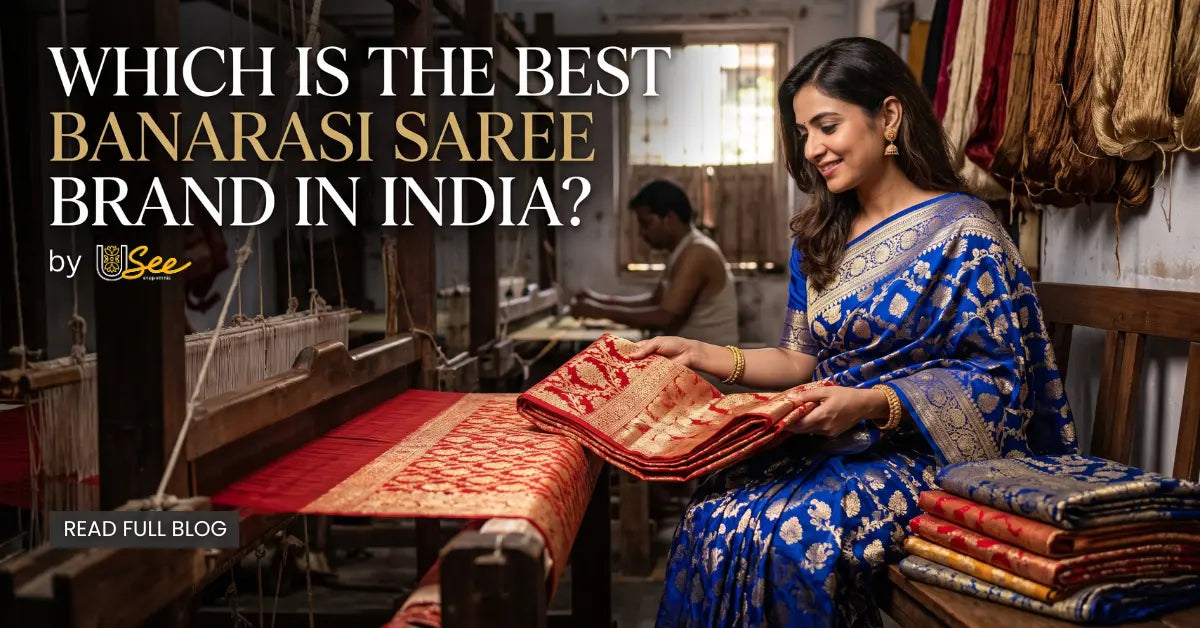 Woman in a royal blue Banarasi silk saree examining a handwoven red Banarasi saree inside a traditional weaving workshop with handloom artisans in India.